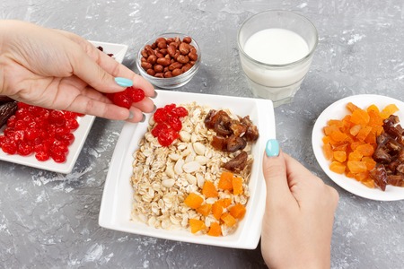 the girl is preparing her muesli for breakfast. The girl puts herself a dried fruit in oatmeal porridge. Useful and healthy breakfast on a gray background, top view.の写真素材