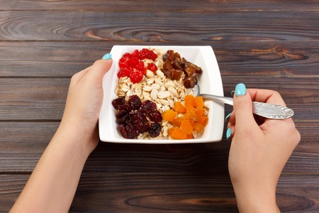 the girl cooked her muesli for breakfast. the girl eats oatmeal porridge that would lose weight and maintain a diet. Useful and healthy breakfast. dark wooden background, top view.の写真素材