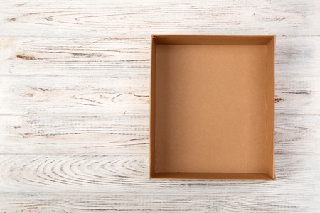 Opened brown blank cardboard box on wooden background, top view.