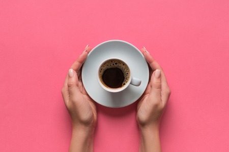 High angle of woman hands holding coffee cup on pink background Minimalistic style. Flat lay, top view isolated.の写真素材