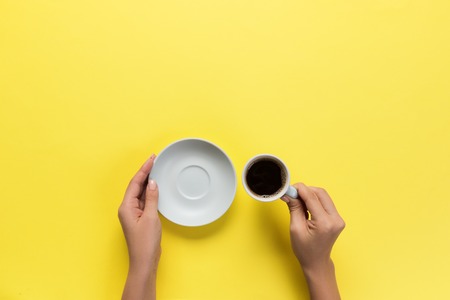 High angle of woman hands holding coffee cup on yellow background Minimalistic style. Flat lay, top view isolated.の写真素材