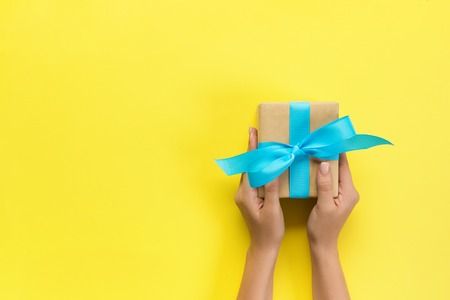 Woman arms holding gift box with blue ribbon on color background, top view.の写真素材