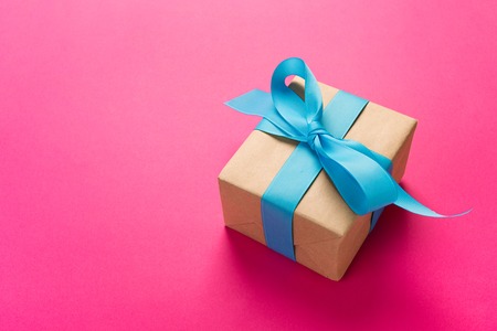 gift wrapped and decorated with blue bow on pink background with copy space. Flat lay, top view.