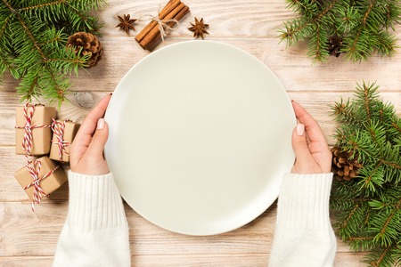 girl hand hold Top view. Empty white plate on wooden background with christmas decoration. New Year concept.の写真素材