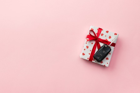 Car key on paper gift box with red ribbon bow and heart on table background. Holidays present top...