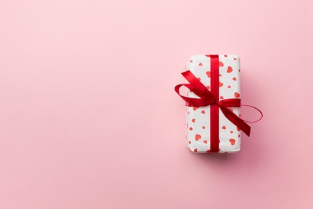 Gift box with red hearts on coral colored background.