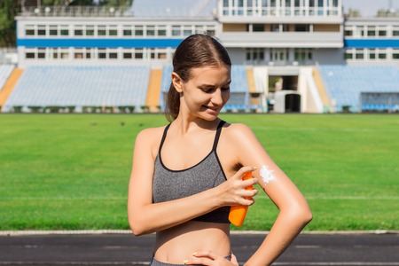 Sporty woman applying sunscreen on stadium before run. Sports and healthy concept.