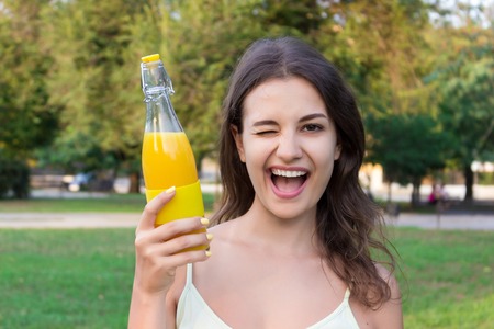 Young girl is walking in the park holding a bottle of fresh cold juice or lemonade in a warm sunny day.の写真素材
