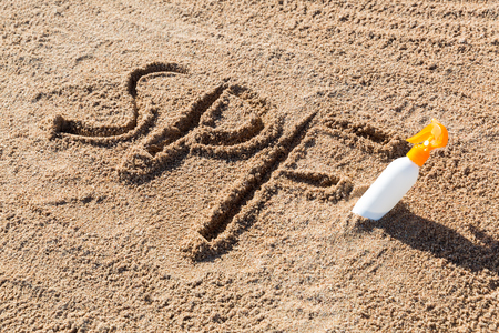 Sun protect factor. SPF word written on the sand and white bottle with suntan cream. Skin care concept background.の写真素材