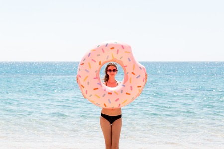 Woman playing with inflatable ring. Girl relaxing on pink inflatable on the beach. Summer holidays...
