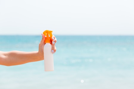 Croped image of woman's hand holding sunscreen spray at the sea background.の写真素材