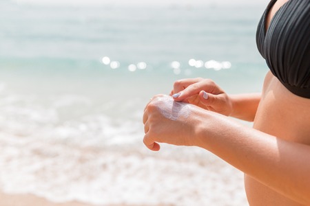 Woman in swimwear is applying sun cream on her hand with her finger at the sea background.の写真素材