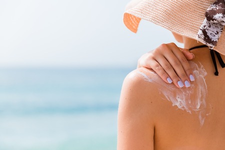 Sunscreen sunblock. Woman in a hat putting solar cream on shoulder outdoors under sunshine on...