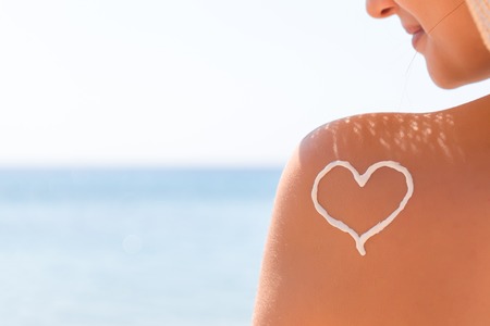 Heart made of sun cream is drawn on woman's shoulder at the beach.