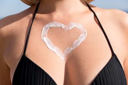 Tanned woman with heart shaped sun cream on her breast at the sea background.の写真素材