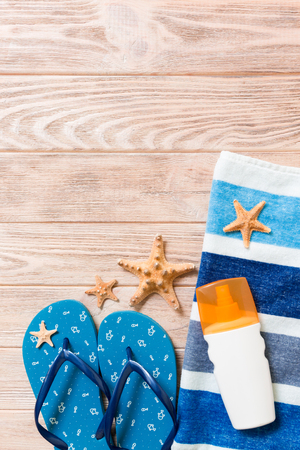 Top view of Beach flat lay accessories. sunscreen bottle with seashells, starfish, towel and flip-flop on wooden board background with copy space.の写真素材