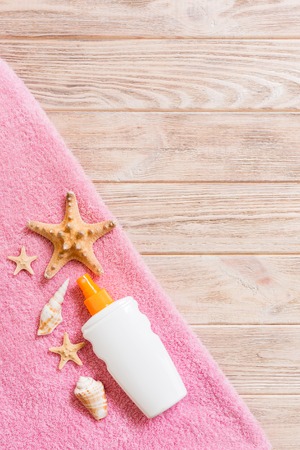 Top view of summer beach staff with copy space. Seashells or seastar, a bottle of suncream and pink towel on wooden background. Summer vacation concept.の写真素材