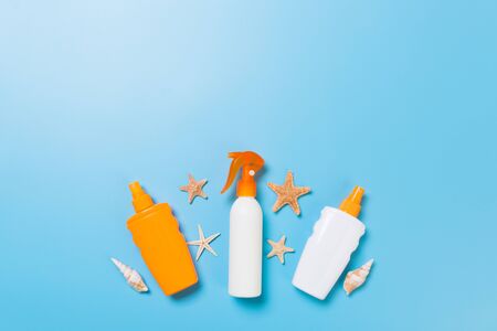 sunscreen cream with starfish and seashells in bottles on blue background, top view.