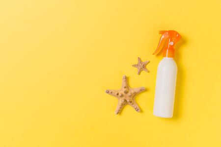 sunscreen cream with starfish and seashells in bottles on yellow background, top view.の写真素材