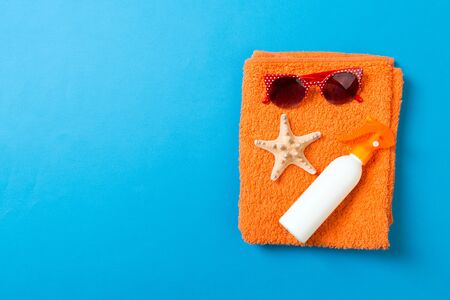 Summer beach flat lay accessories. Sunscreen bottle cream, towel and seashells on colored...