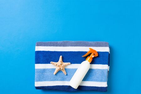 Summer beach flat lay accessories. Sunscreen bottle cream, towel and seashells on colored...