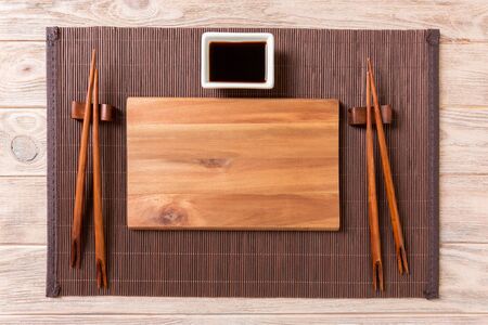 Empty rectangular wooden plate for sushi with sauce and chopsticks on wooden table, top view.の写真素材