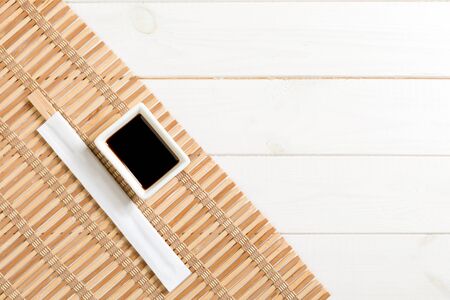 Bamboo mat and soy sauce with sushi chopsticks on white wooden table. Top view with copy space background for sushi. Flat lay.の写真素材
