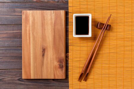Empty rectangular wooden plate with chopsticks for sushi and soy sauce on wood background. Top view with copy space.の写真素材