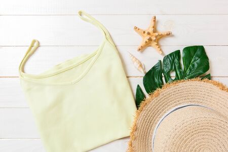 Summer accessories with t-shirt, seashells and straw hat on white wooden background top view flat lay.の写真素材