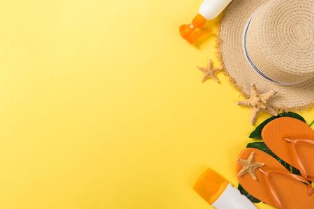 Beach accessories with straw hat, sunscreen bottle and seastar on yellow background top view with...