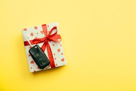 Give gift car key concept top view. Present box with red ribbon bow, heart and car key on yellow colored background.の写真素材