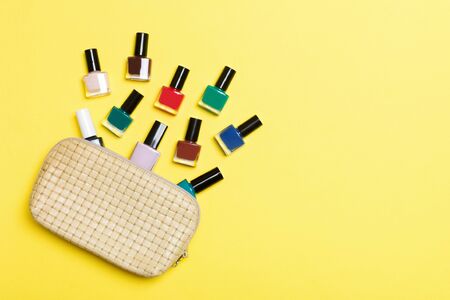 Top view of cosmetics bag with fallen out colourful nail polishes on yellow background. Beautiful nails concept with empty space for text.の写真素材
