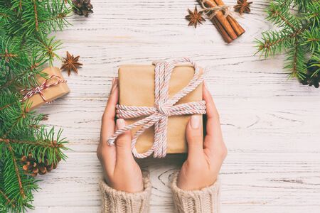 Female hands holding handmade present box in recycled paper on white wooden table background. christmas preparation concept, Gift wrapping background. Toned.の写真素材