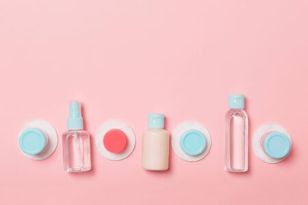 Top view of means for face care: bottles and jars of tonic, micellar cleansing water, cream, cotton pads on pinkbackground. Bodycare concept with empty cpace for your ideas.の写真素材