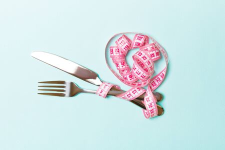 Top view of obesity concept with fork and knife wrapped in curled measuring tape on blue background...