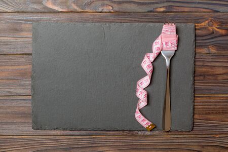 Strict diet concept with empty space fro your design. Top view of plate with fork in measuring tape on wooden background.の写真素材