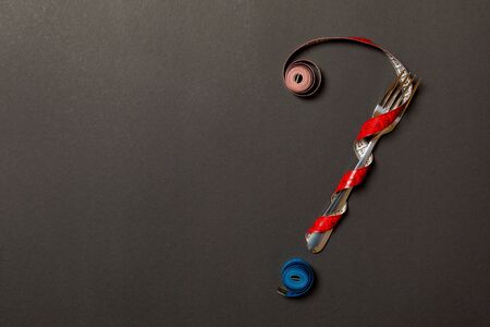 Top view of question mark made of fork and measuring tape on black background. Diet concept with...