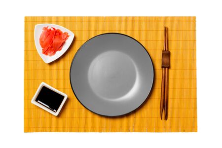 Empty round gray plate with chopsticks for sushi and soy sauce, ginger on yellow bamboo mat background. Top view with copy space for you design.の写真素材