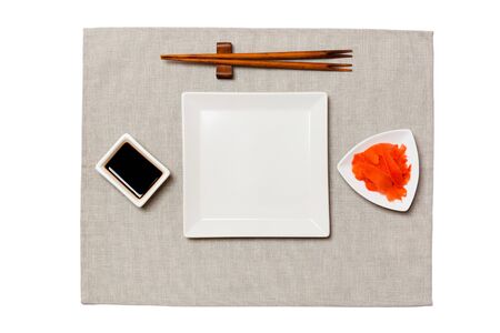 Empty white square plate with chopsticks for sushi, ginger and soy sauce on grey napkin background. Top view with copy space for you design.の写真素材
