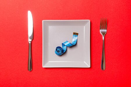Measuring tape in a plate with fork and knife on both sides on red background. Top view of weight loss concept.の写真素材