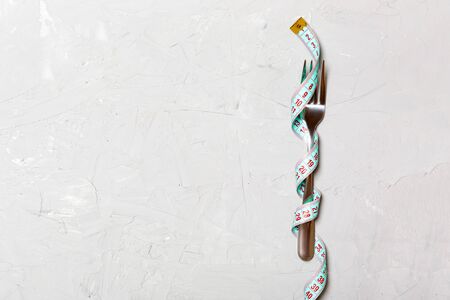 Top view of wrapped fork in tape measure on gray background with space for your ideas. Healthy eating and diet concept.の写真素材