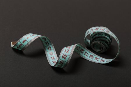 Perspective view of curled measure tape on black background. Keeping fit concept.