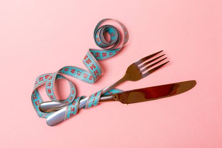 Composition of curled measuring tape, fork and knife on pink background with empty space for your...