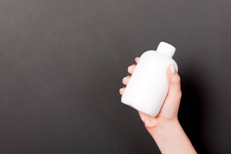 Female hand holding cream bottle of lotion isolated. Girl give tube cosmetic products on black...