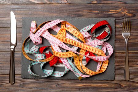 Top view of heap of colorful measuring tapes in plate on wooden background. Diet concept with copy space.の写真素材