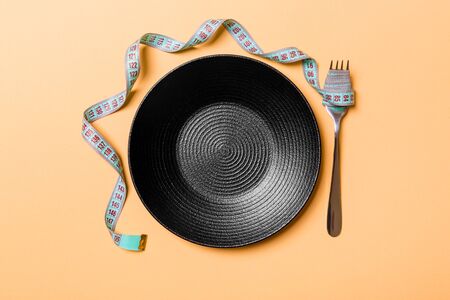 Strict diet concept with empty space fro your design. Top view of plate with fork in measuring tape on orange background.の写真素材