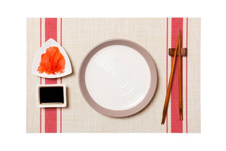 Empty round white plate with chopsticks for sushi and soy sauce, ginger on sushi mat background. Top view with copy space for you design.の写真素材