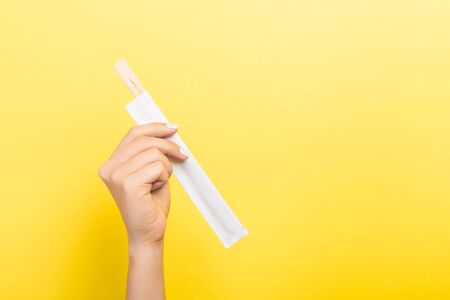 Woman's hand holding chopsticks in a pack on yellow background. Chinese food concept with empty space for your design.の写真素材