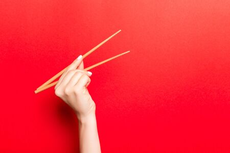 Creative image of wooden chopsticks in female hand on red background. Japanese and chinese food with copy space.の写真素材