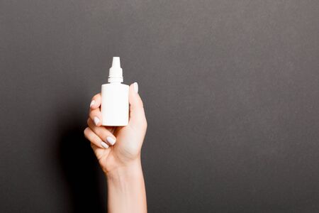 Female hands hold medicine bottle nose spray on Black background isolation.